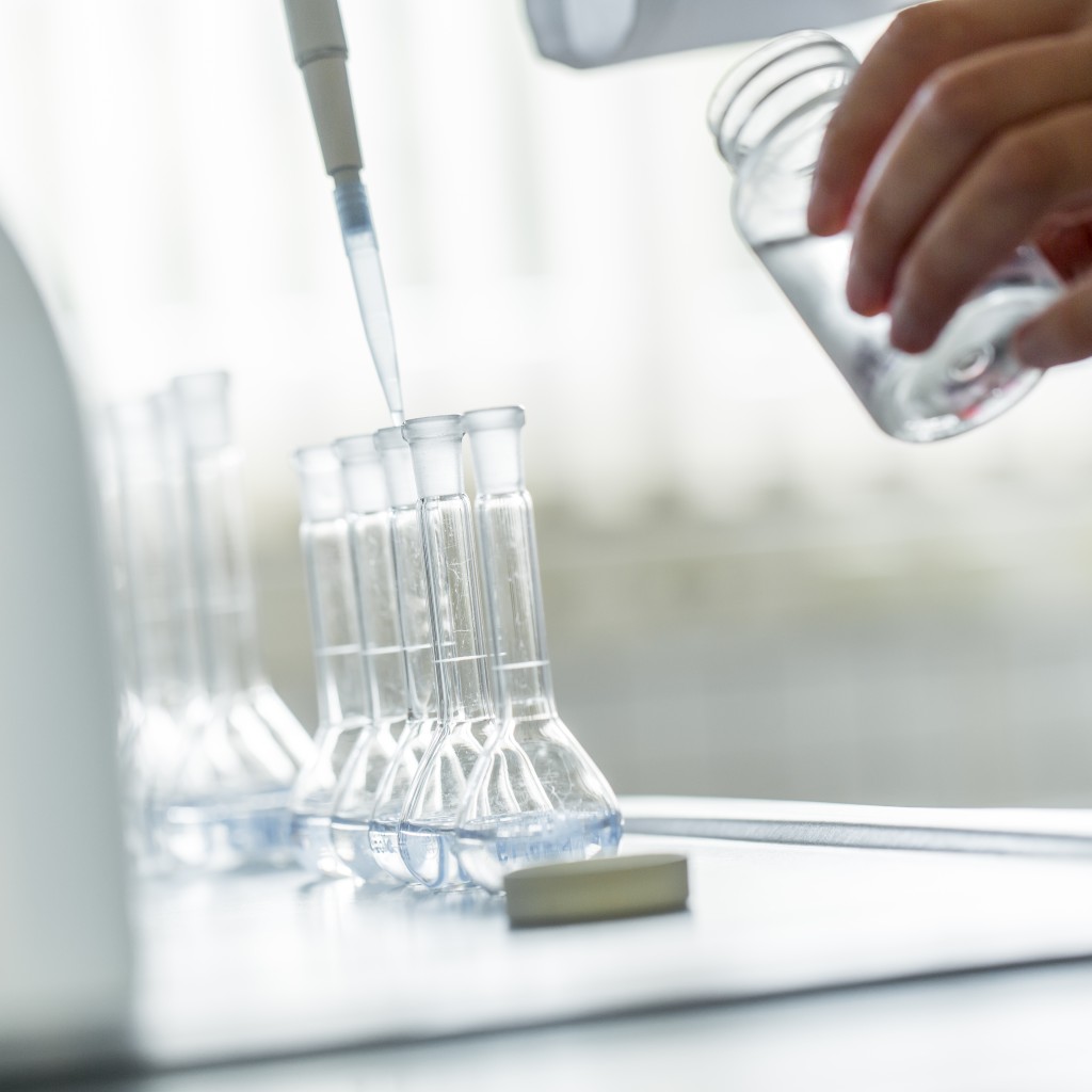 Eine Person tropft Flüssigkeit mit einer Pipette in Reagenzgläser.