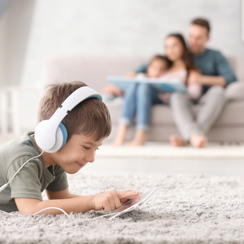 Ein Junge nutzt zu Hause das WLAN auf seinem Tablet, während seine Familie im Wohnzimmer zusammen sitzt und ein Buch anschaut.