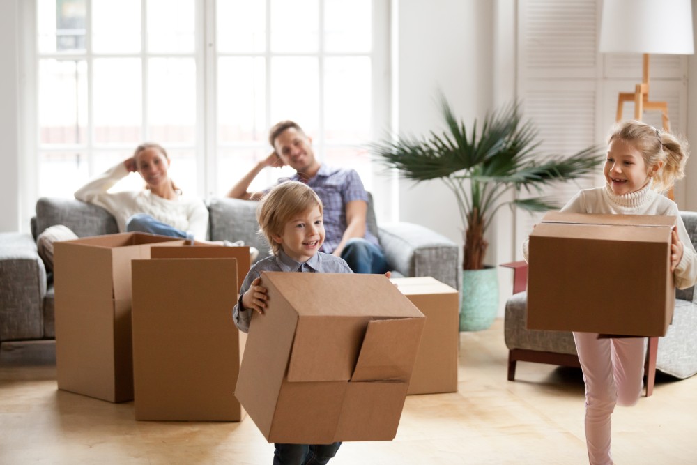 Familie beim Umzug. Kinder rennen glücklich mit einem Karton durch das Wohnzimmer.