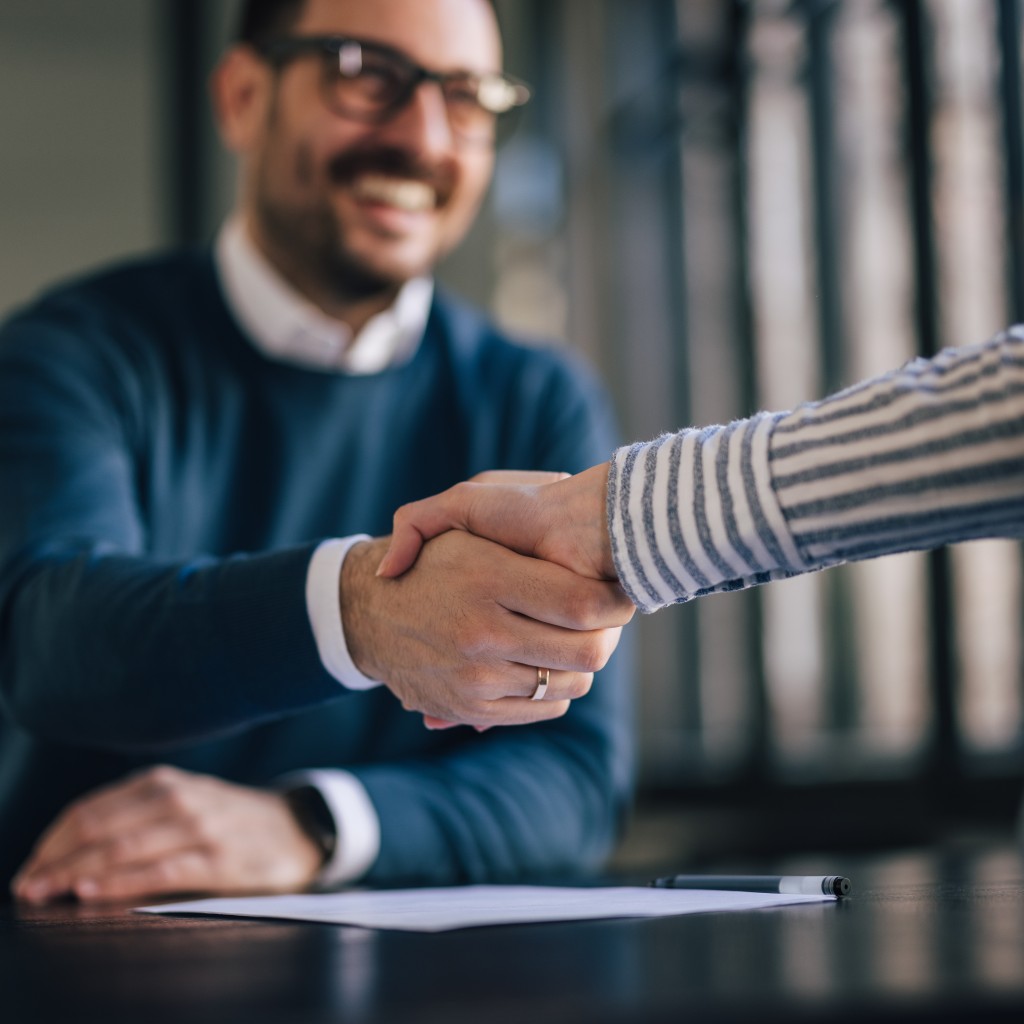 Business Meeting. Personen am Tisch reichen sich die Hände.