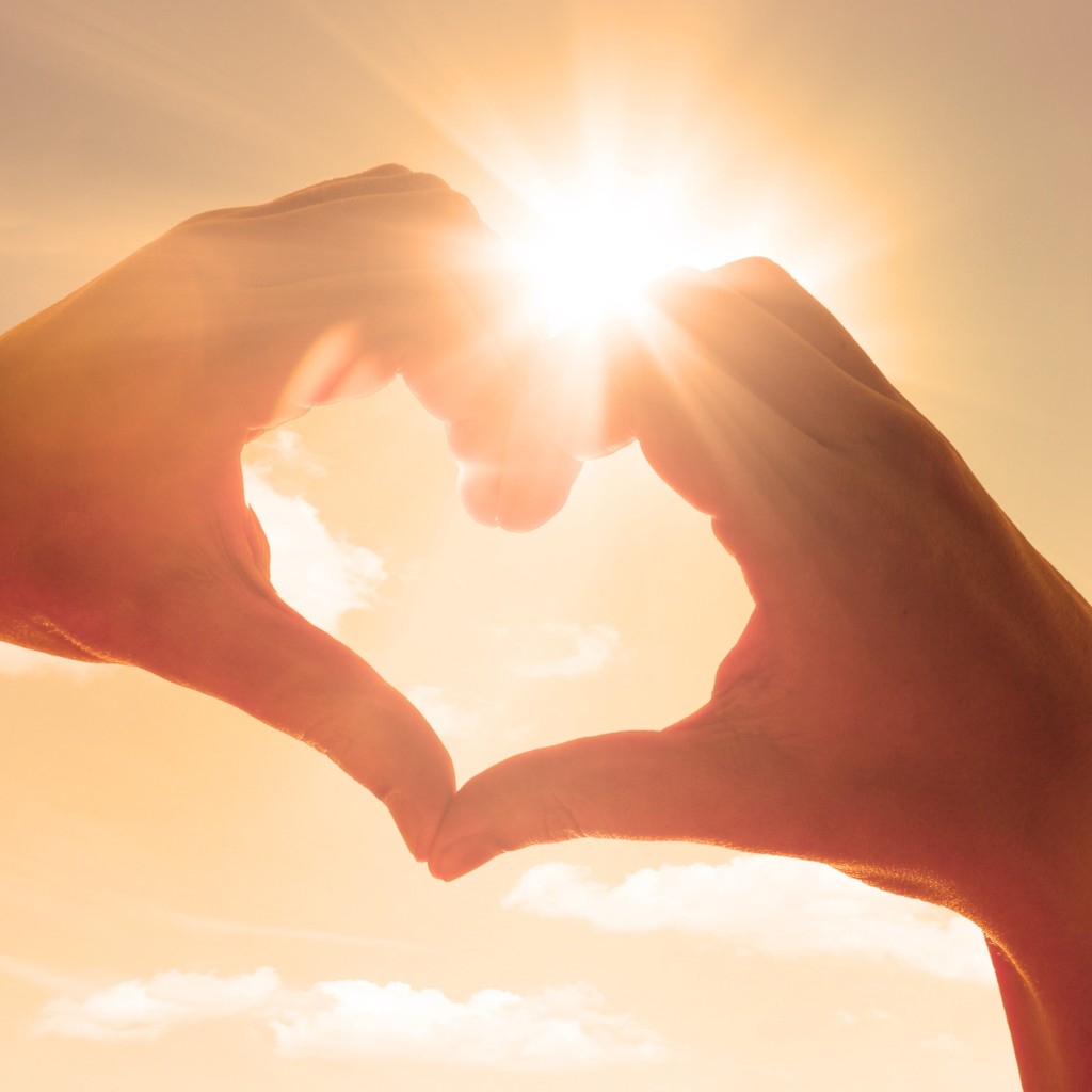 Hände zum Herz geformt. Sonne scheint.